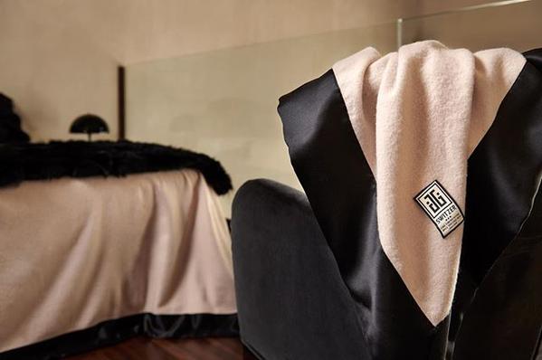 Close up of the camille cashmere blend blanket with pure black silk 4 inch borders hanging off a chair with a bed in the background