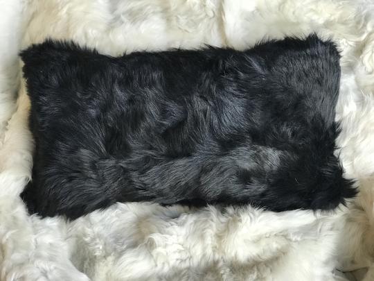 Small rectangular black real Toscana sheepskin fur pillow lying on top a white fur blanket