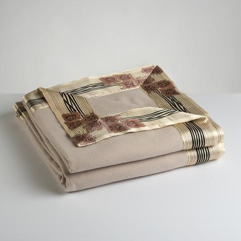 Now Voyager luxury throw blanket in champagne beige lying folded with signature gold rose motif borders.