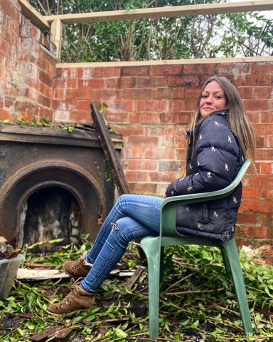 Danni sitting by a Victorian shed, with foliage around her feet