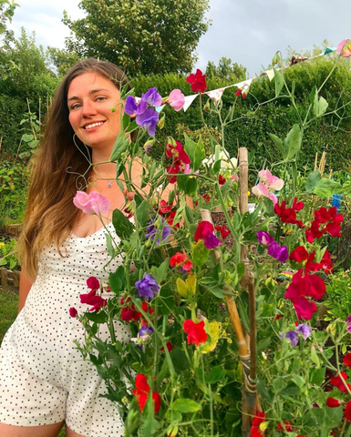 Rachel, smiling, standing beside a flowering plant