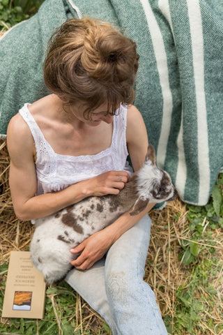 Blonde woman holding a speckled lamb sitting on Topsy Farms' green wool blanket