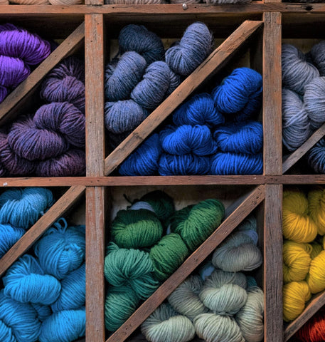 Close up of blue, green, yellow, and purple Topsy Farms' yarn on wooden shelving