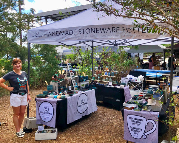 Camille Woodward standing in front of pottery booth tent at a festival.