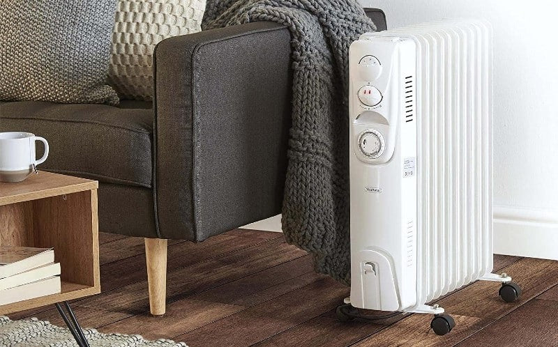 White Oil Filled Radiator next to a grey sofa on a brown hardwood floor