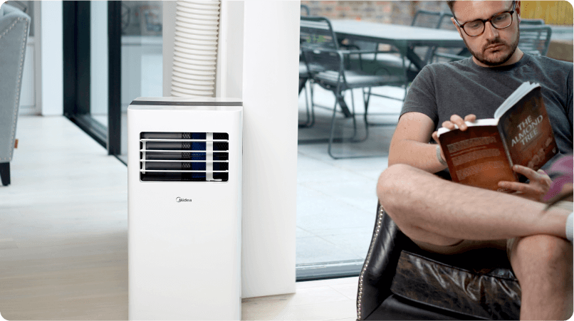 an image of a man sitting on a couch while reading a book next to an air conditioning unit