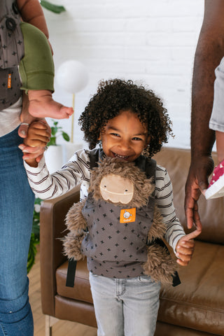 Una bambina tiene per mano i suoi genitori e porta con sé il suo marsupio per bambole di Tula.