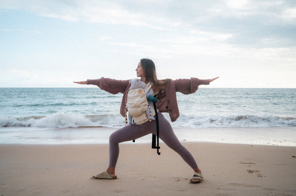 Mamma che fa yoga su una spiaggia con un bambino nel marsupio 
