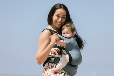 Une mère utilisant un porte-bébé de voyage Tula Lite en été.