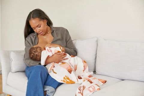 A mother is breastfeeding with a baby tula blanket.