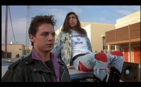 screen shot from movie Heathers, featuring two teenage boys, one wears a t-shirt that says "something to prove"