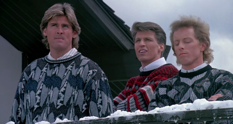 three white men wear patterned sweaters and have feathered hairstyles, and stand outside in the snow