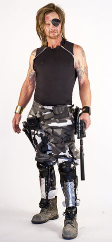 man with long hair holds a gun and wears an eyepatch, a black tank top with zipper shoulders, and gray camo pants