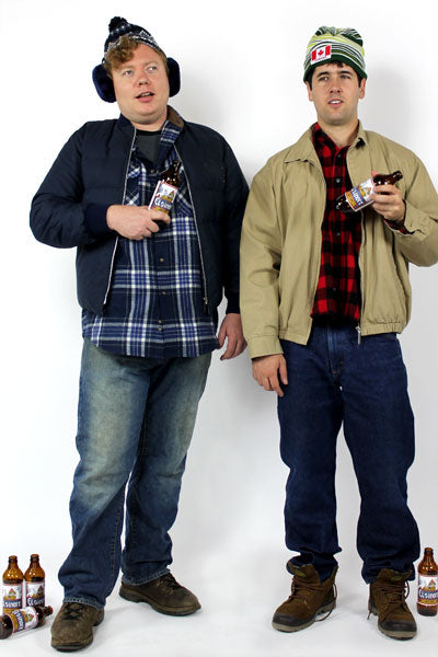 two men wearing plaid shirts, jeans, boots, jackets and wearing stocking caps and holding beer bottles
