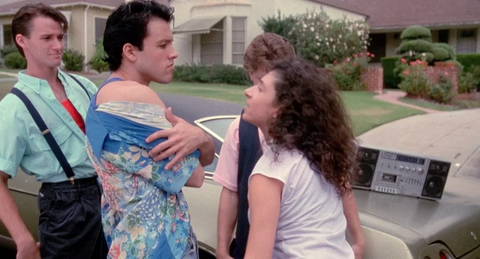 two teenagers face off on a suburban street, one is wearing a white tank and one a blue tank with a button up shirt over it