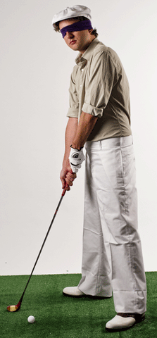 a man wears a white cap, brown shirt, white pants and has a blindfold on and has a golf club