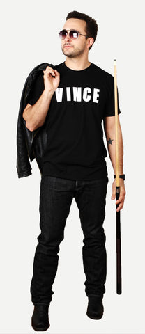 a man wears sunglasses, a black t-shirt that says vince on it, black pants, and carries a leather jacket and pool cue