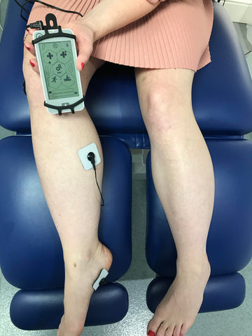 Lady in a Podiatrists office using the NuroKor mitouch device to treat her right foot and knee.