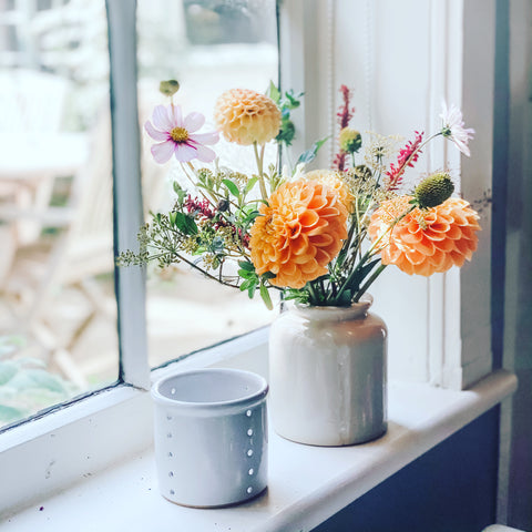 A pot of dahlias sits on a cottage window sill next to a handmade tealight holder