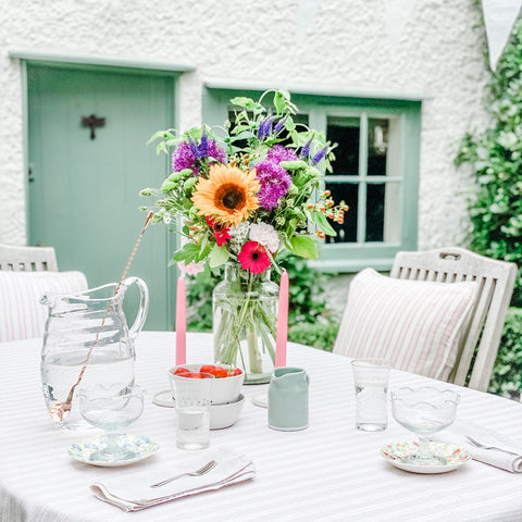 A summer garden table laid with cushions, tablecloth and flowers