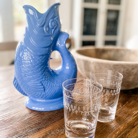 A sea blue gluggle jug on a wooden table with two tumblers from The Vintage List