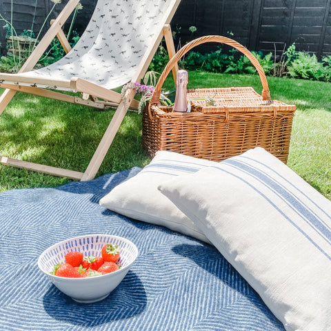 A picnic blanket with cushions and a wicker picnic basket