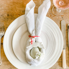 An egg within bunny ears napkin tied with a lovely handmade ceramic hare