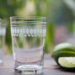 A hand blown and hand engraved tumbler on a table with a chopped slice of lime nearby