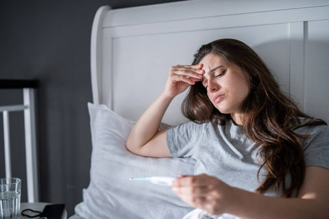 A woman in her bed with a fever holding thermometer