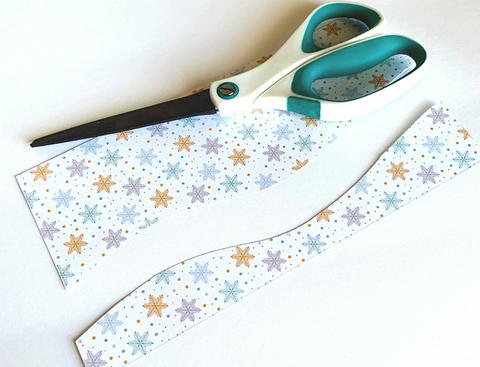 scissors shown over snowflake scrapbook paper cut to create wavy hills and valleys