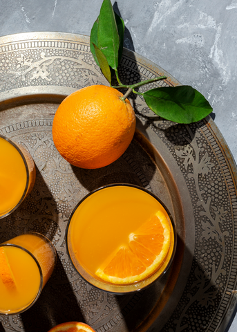 Glasses of orange juice on a decorative platter with an orange and orange slice