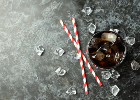 glass of cola with ice and two straws on table with ice cubes