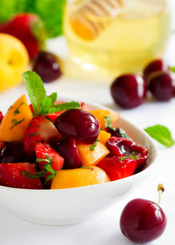 Fruit salad in bowl and jar of honey in background