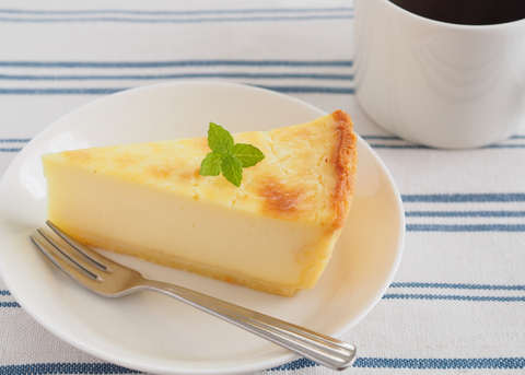 slice of cheesecake with mint garnish on a plate with a small fork with a cup of coffee on the side