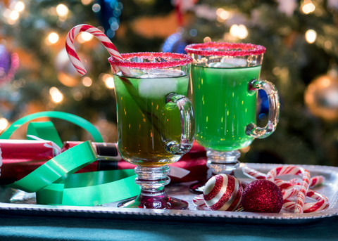 Two Grinch cocktails with red sugar rim and candy cane garnish with Christmas Tree in background