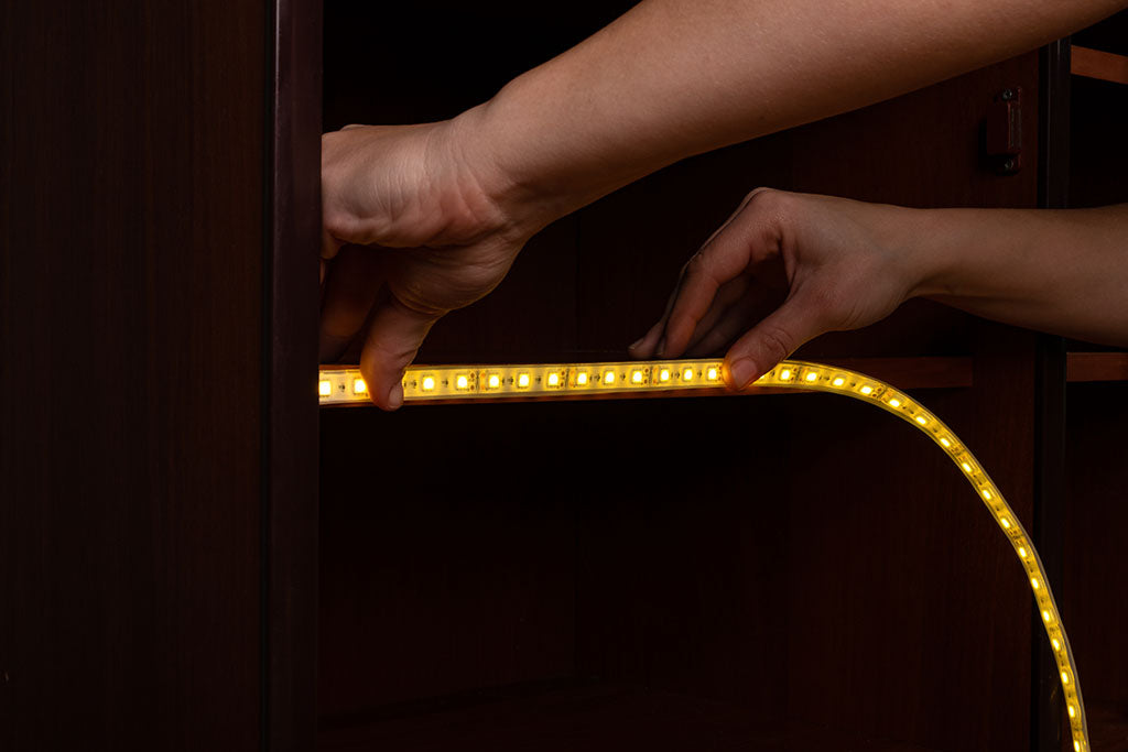 A person's hands applying LED strip lights to a wooden surface