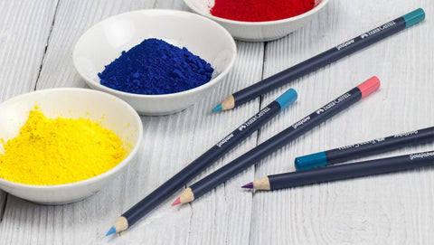 Goldfaber Color Pencils next to bowls of pigment in yellow, blue, and red.