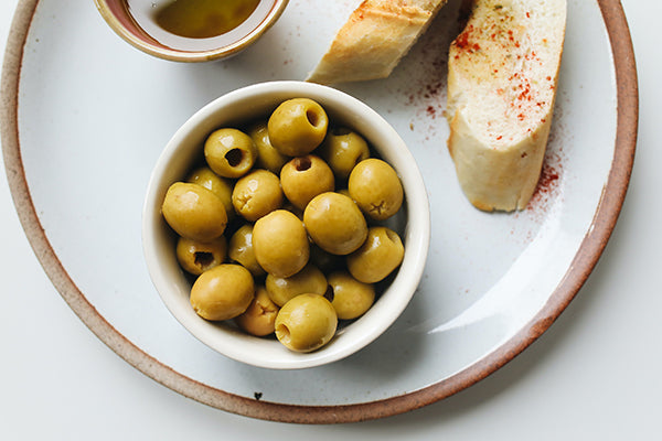 A bowl of olives paired with bread and wine.