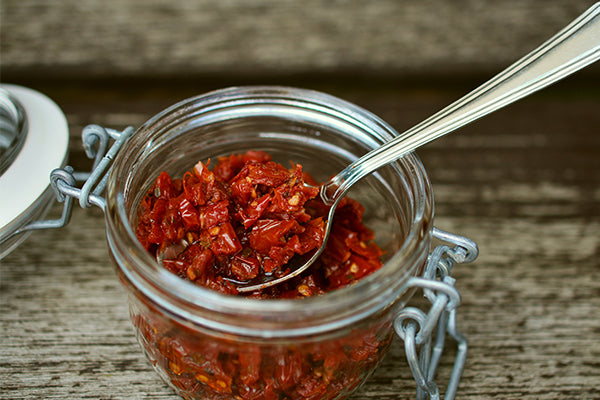 Sun-dried tomatoes in a jar with a spoon to serve.