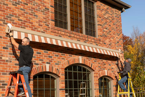 Two Men on Ladders Installing Home Awning on Brick House