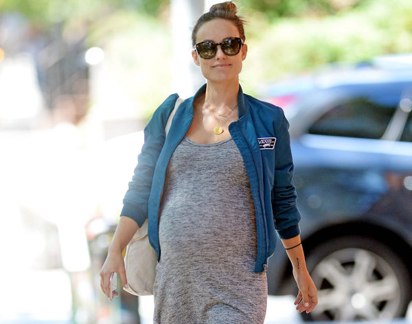 Olivia Wilde walking down the street pregnant in grey dress and demin jacket.