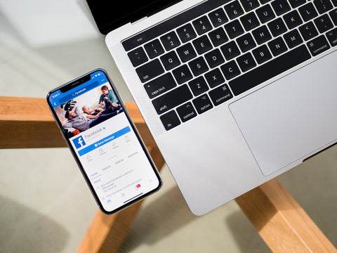 Facebook social media on phone next to laptop