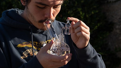 Image within 'The Ultimate Guide to Pipe vs Bong for Smoking Weed' on The Dart Company's blog, depicting a person smoking from a bong to emphasize the enhanced filtration and flavor benefits in the 'Pipe vs Bong' comparison.