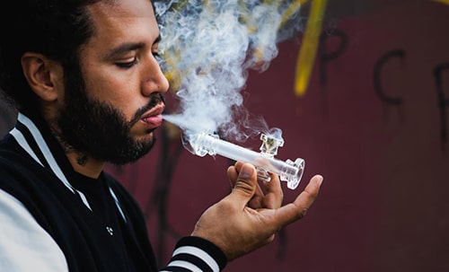 Image featured in 'The Ultimate Guide to Pipe vs Bong for Smoking Weed' on The Dart Company's blog, depicting a person smoking from a pipe to emphasize the convenience of on-the-go smoking within the 'Pipe vs Bong' comparison.