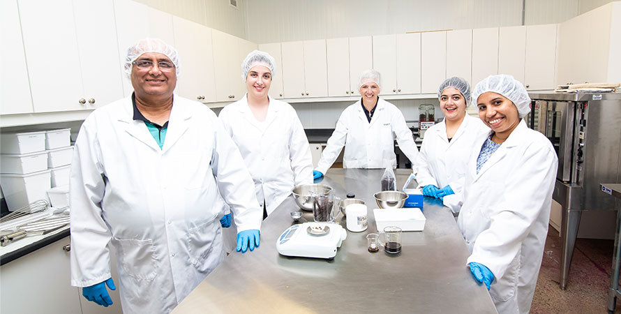 A group of people wearing food safety protective clothing standing around a steel table