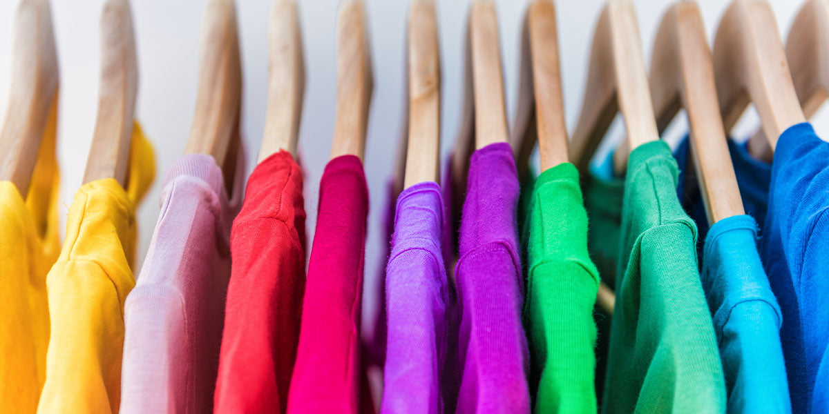 Fashion clothes on clothing rack - bright colorful closet. Closeup of rainbow color choice of trendy female wear on hangers in store closet or spring cleaning concept.