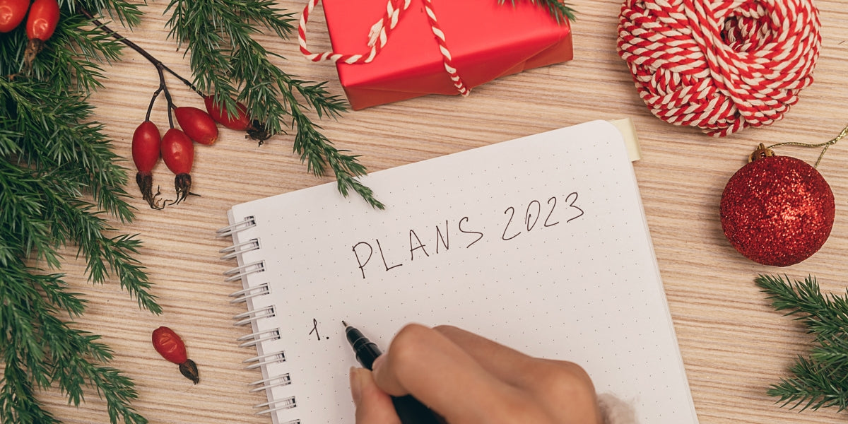 A woman writing plans for 2023 in a notebook, hands close-up, top view.Holiday decorations.New Year and Christmas concept.Planning concept.