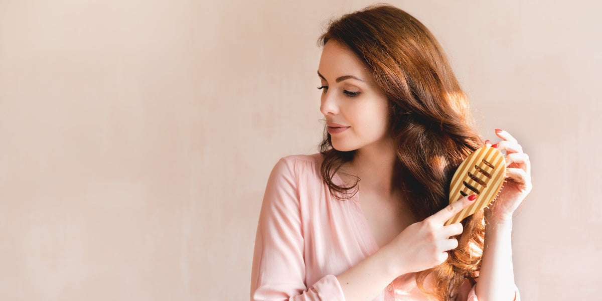 Beautiful young woman combing brushing her long smooth hair with a wooden comb. Haircare concept.