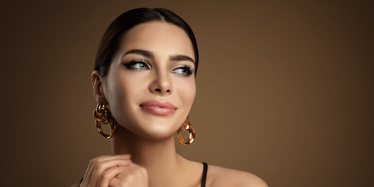 Beauty Model Portrait with plump Lip Makeup looking sideways. Beautiful smiling Woman with smooth Face Skin Make up and Golden Earrings over brown. Dermal Filler