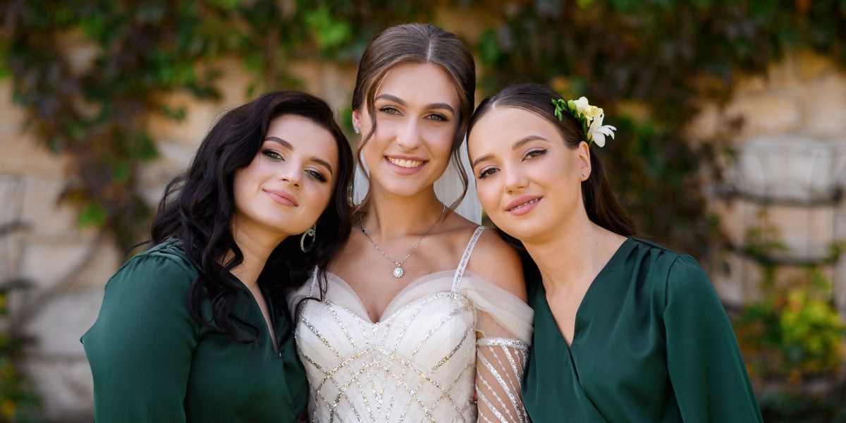 Cheerful elegant bride young woman posing with two bridesmaids in dark green dress standing outdoors. Attractive woman in wedding dress with long sleeves. Celebration of wedding. Friends of bride.